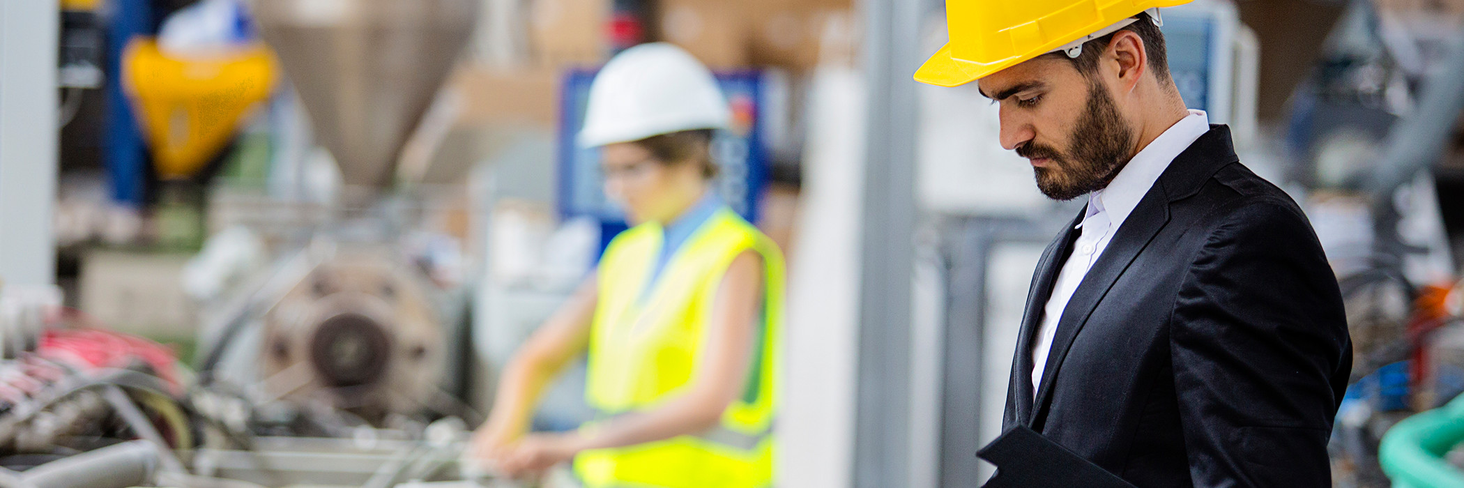 Man in suit and hard hat and woman in hard hat on engine fabrication line