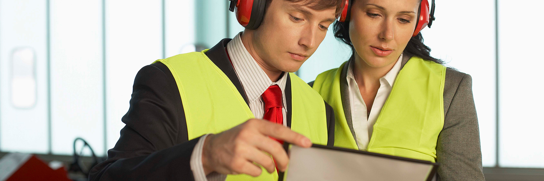 Two businesspeople consulting while wearing safety earmuffs and vests