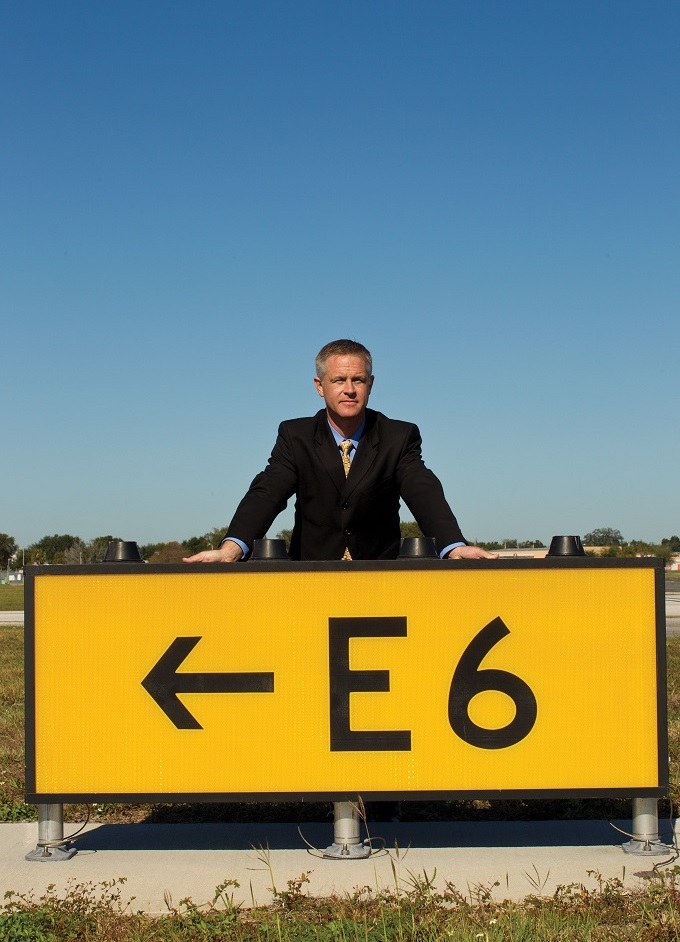 Man standing behind airport runway sign