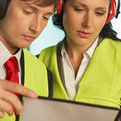 Two businesspeople consulting while wearing safety earmuffs and vests