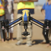 Drone hovering low over beach with operating crew in background