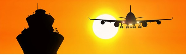 Silhouette of anairplane flying near an traffic control tower backlit by the sun