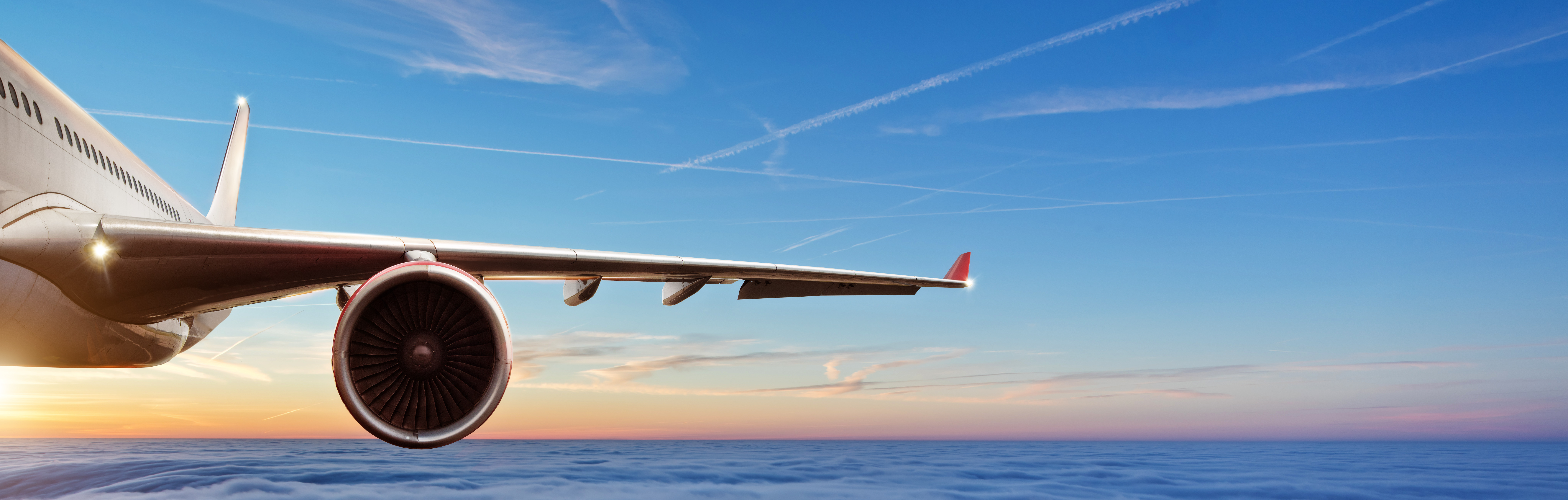 Detail of wing of commercial airplane jetliner flying above clouds in beautiful sunset light.