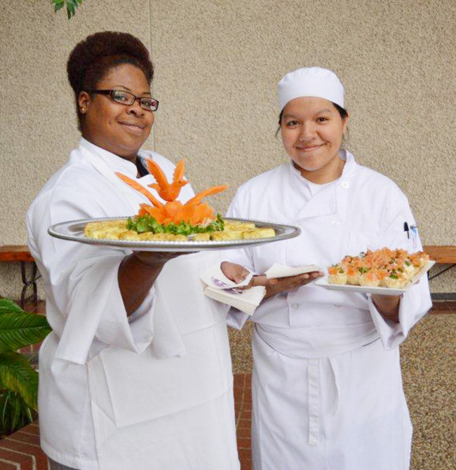 Two female chefs holding plates;